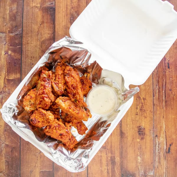 Spicy IPIZZA chicken wings and a dipping sauce in a takeout container on a wooden table.
