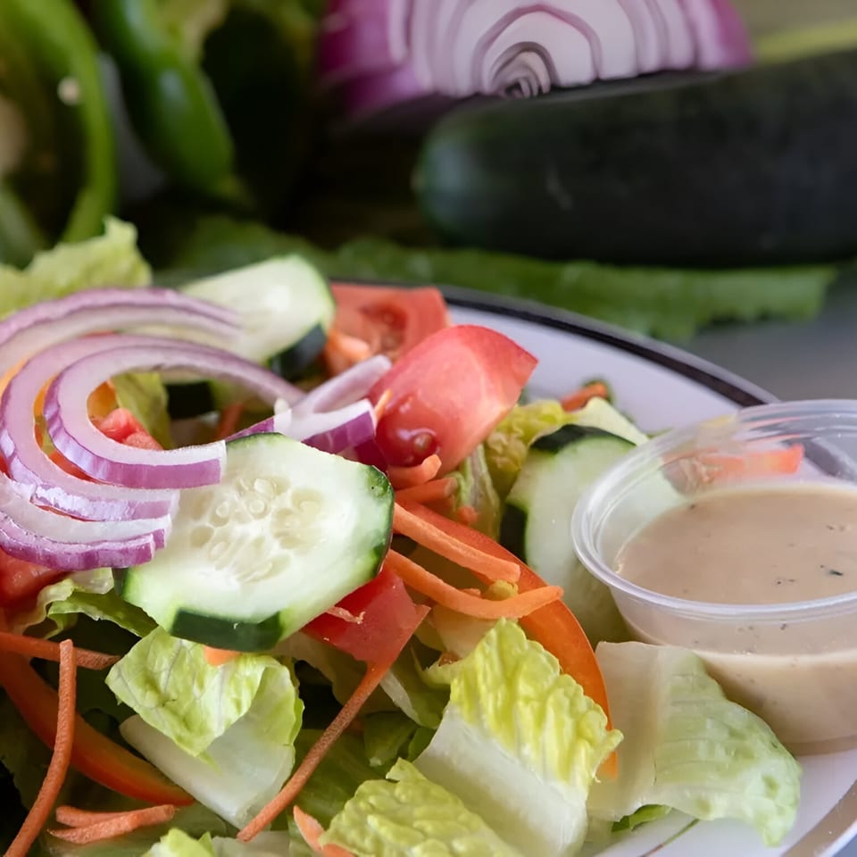 Fresh garden salad with lettuce, tomatoes, cucumbers, red onions, and a side of dressing.