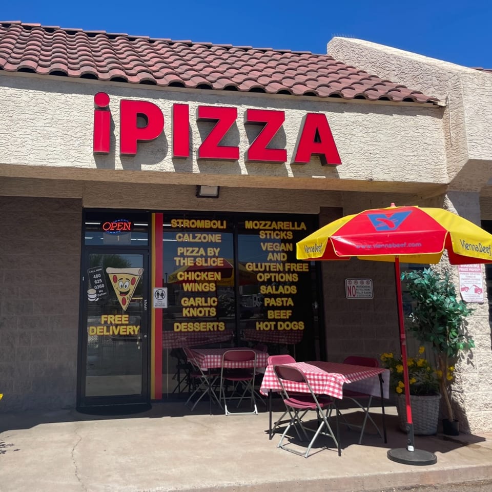 The iPizza restaurant exterior features red signage, outdoor seating with checkered tablecloths, and a Vienna Beef umbrella.