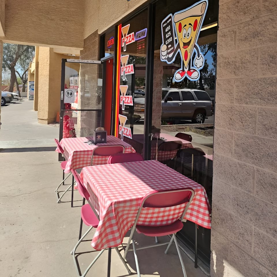 Outdoor seating at IPIZZA Restaurant with red and white checkered tablecloths and a pizza mascot on the window.