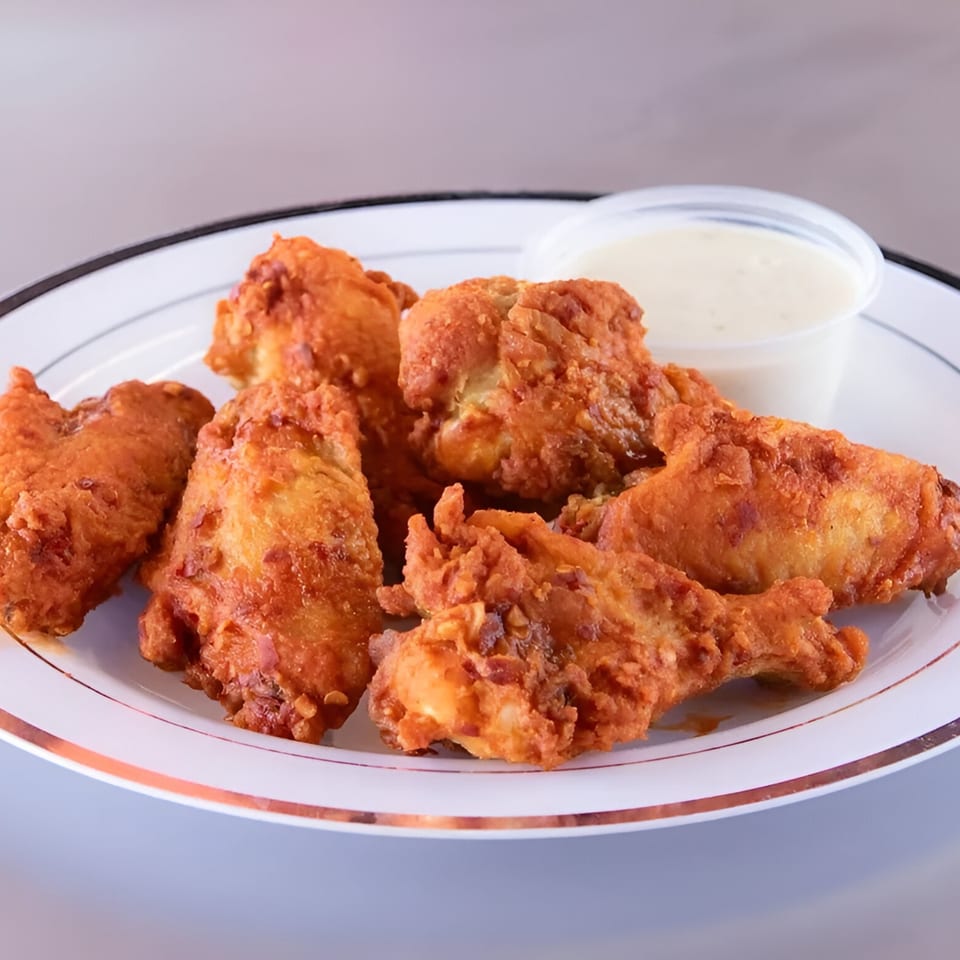 A plate of crispy fried chicken pieces with a side of creamy dipping sauce.