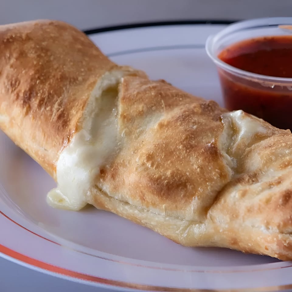 A golden-brown IPIZZA breadstick with melted cheese oozing out, served with a side of marinara sauce.