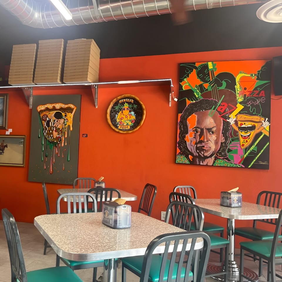IPIZZA Restaurant interior with orange walls, colorful pizza-themed art, and retro diner-style tables and chairs.