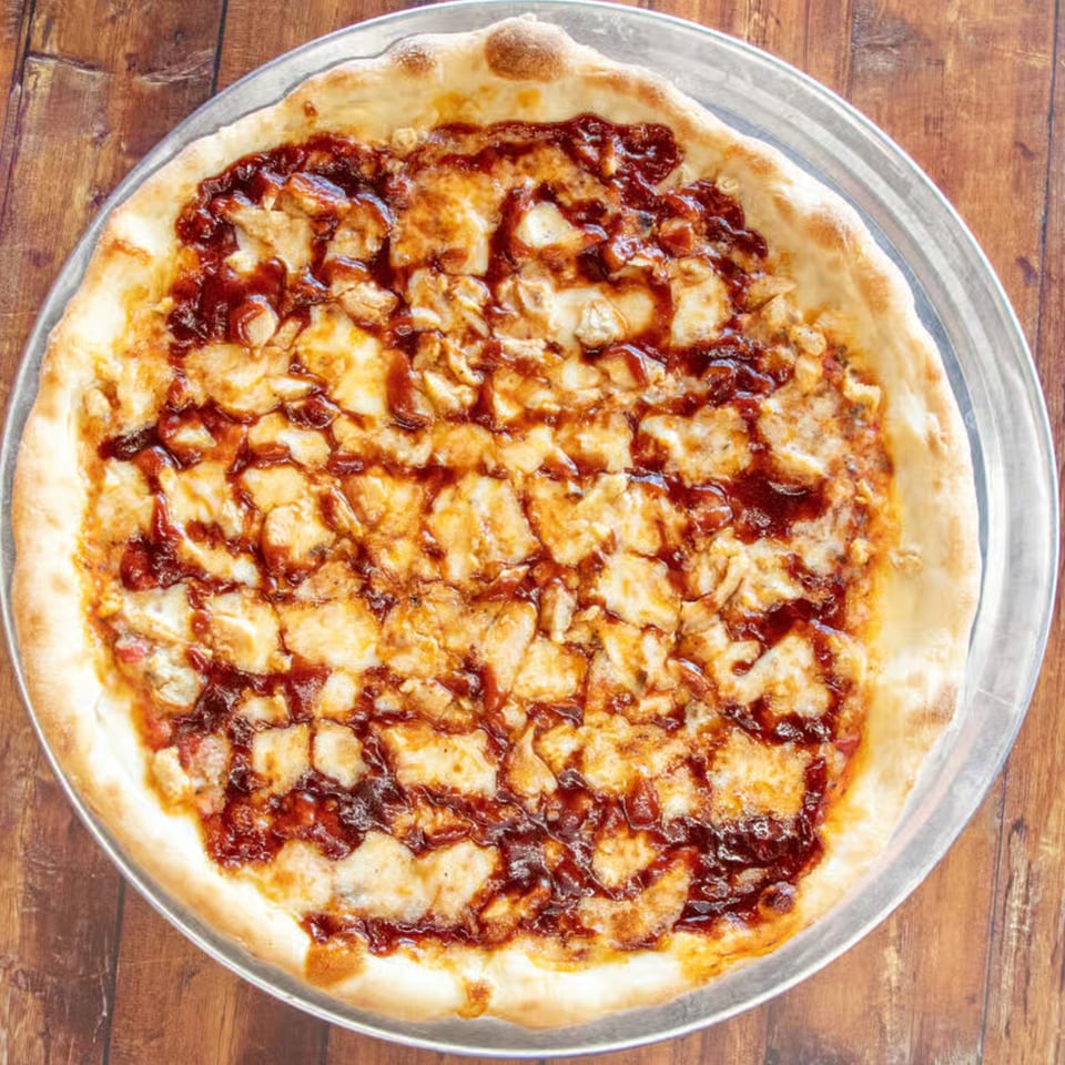 Overhead view of a BBQ chicken pizza with melted cheese and dark sauce on a metal pan.